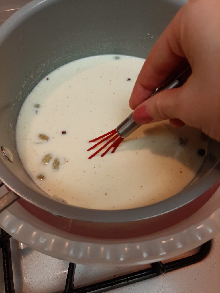 Making cardamom panna cotta, cream, milk, cardamom, cloves, and cinnamon stirred slowly in a pan.