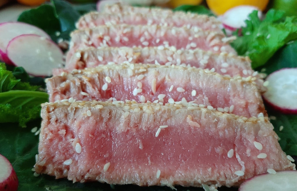 Sesame crusted Seared Ahi Tuna on a bed of Mustard Greens and Collards with Radishes for garnish.