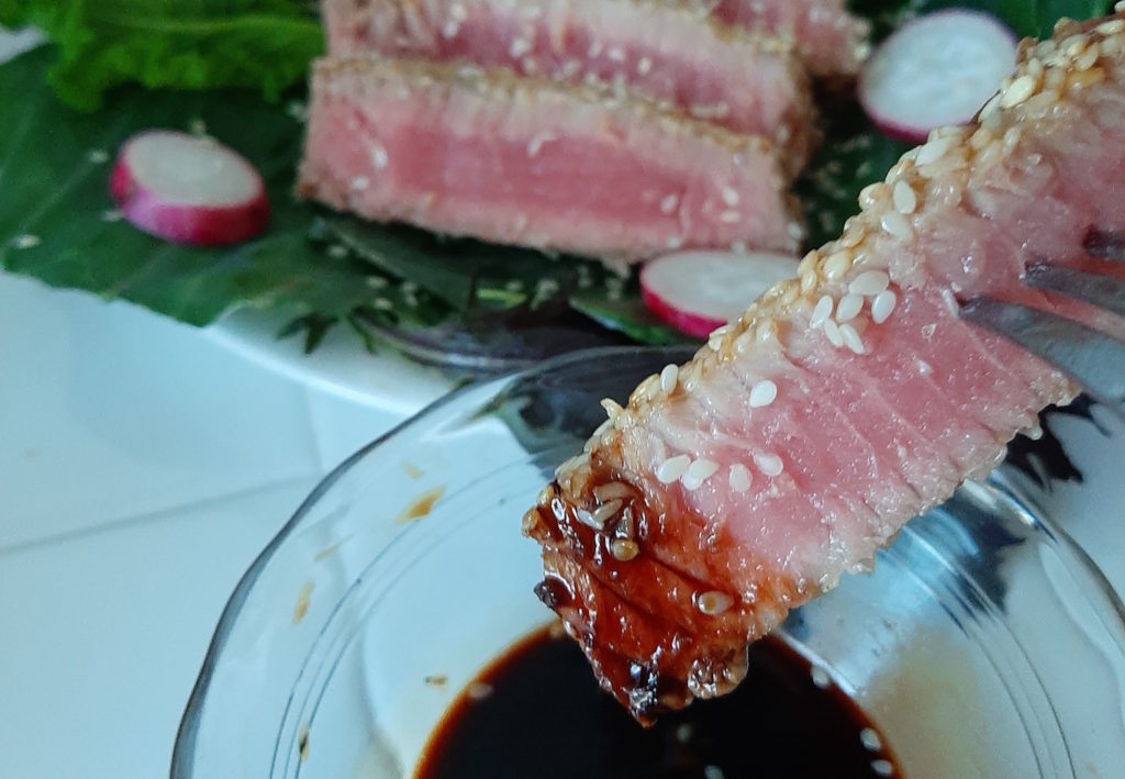 Sesame crusted Seared Ahi Tuna on a bed of Mustard Greens and Collards with Radishes for garnish with one piece dipped in Tamari Sauce