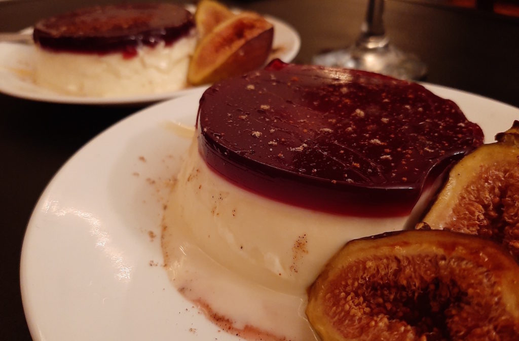 cardamom panna cotta with port wine gelee sprinkled with cardamom and served with honey roasted figs on a white plate, a second plate in the background. all on a black surface. Sugar with Spice Blog.