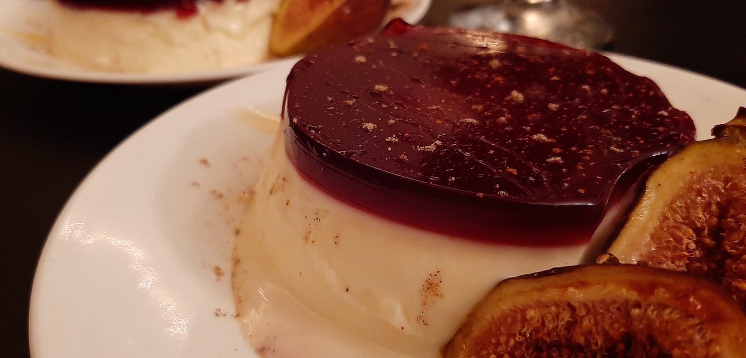 cardamom panna cotta with port wine gelee sprinkled with cardamom and served with honey roasted figs on a white plate, a second plate in the background. all on a black surface. Sugar with Spice Blog.