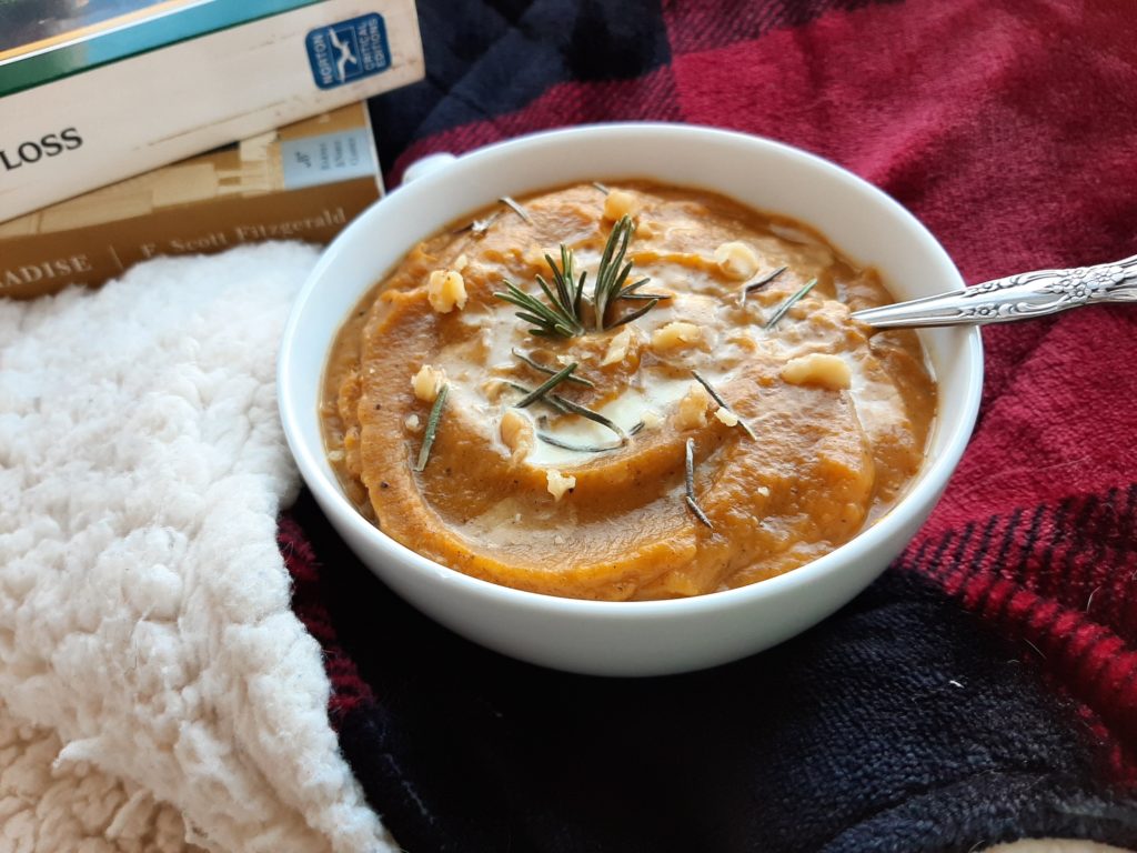 Brown butter butternut squash soup with cream, walnuts, and rosemary in a window seat with a red plaid blanket and books. A cozy Sunday.