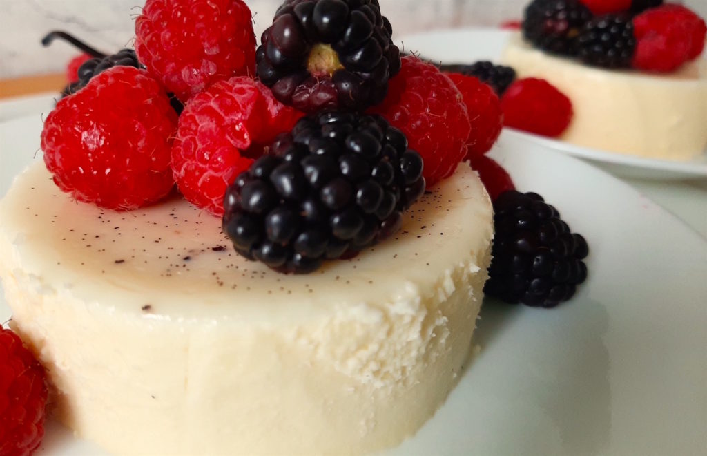 Vanilla Bean Panna Cotta with fresh Raspberries and Blackberries. Vanilla bean and more fresh berries in the background.