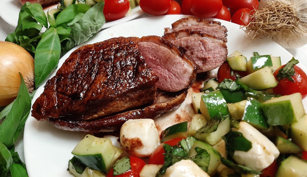 Pan Seared Duck Breast, medium rare duck with a red wine reduction glaze. Served with a caprese salad of tomatoes, basil, olive oil, pepper, and cucumbers.