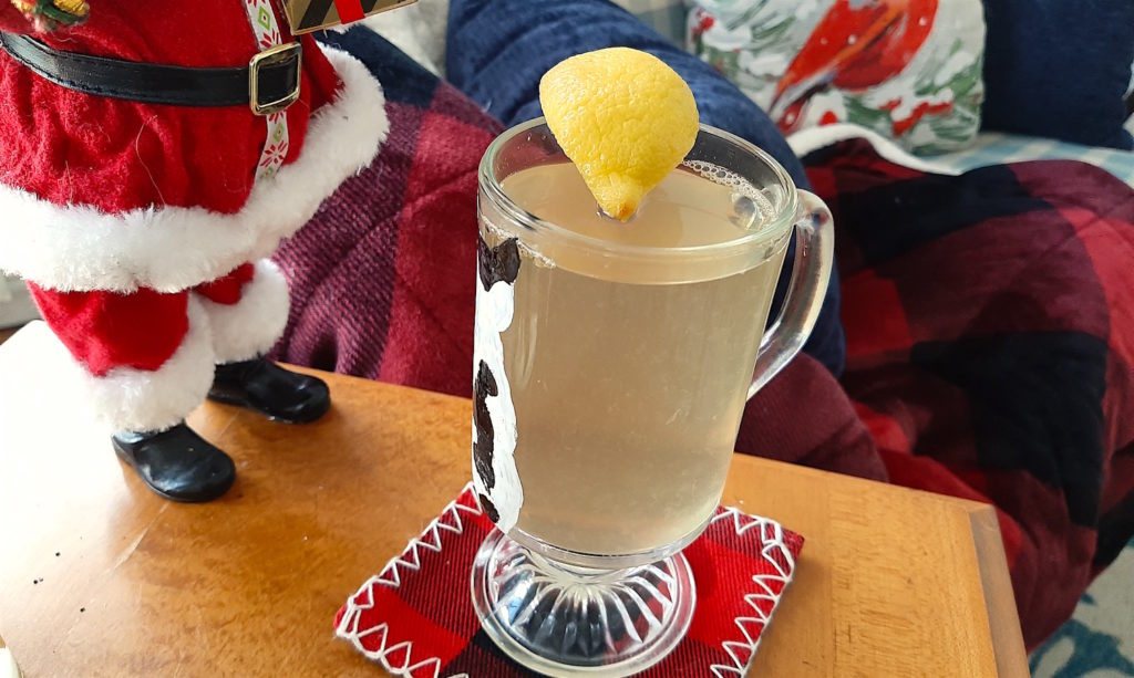 Hot Toddy made with Jameson Irish Whiskey, Honey, Lemon, and hot water, Christmas Cocktail, cozy and warm drink show with red plaid accessories next to a cozy couch and santa decoration