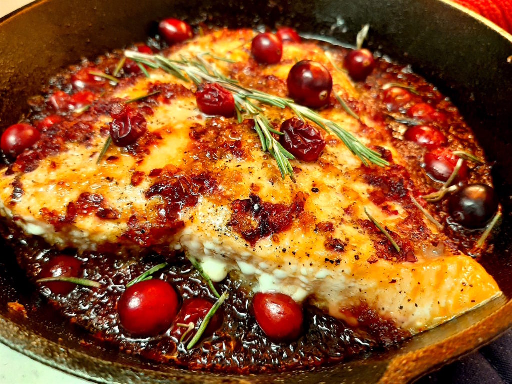 Cranberry Balsamic Salmon in a cast iron skillet with rosemary and fresh cranberries. A lovely fall dinner that makes left overs so you don't have to cook the next night!