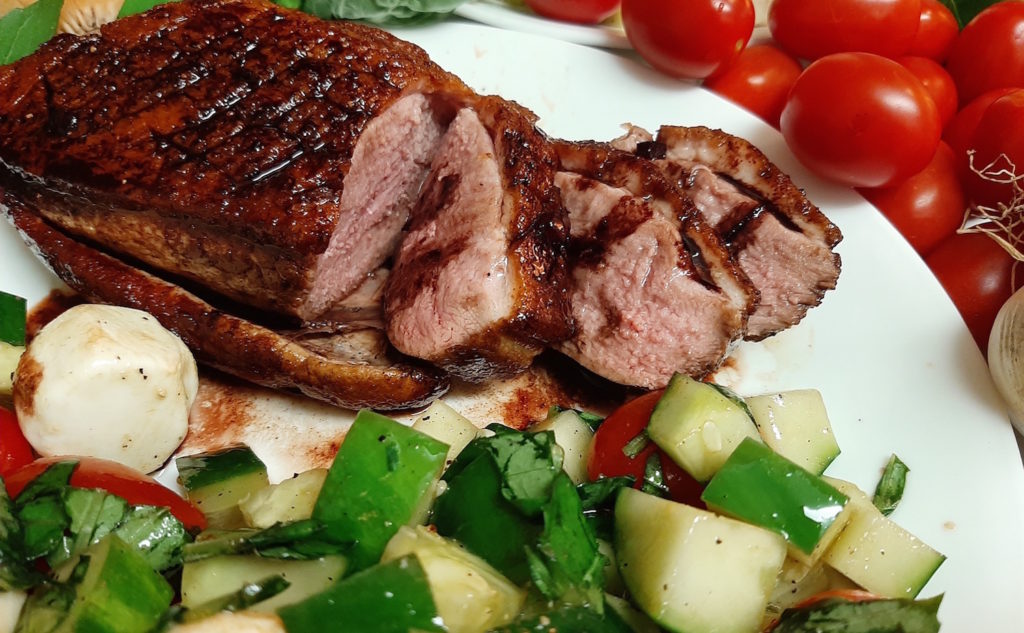 Pan Seared Duck Breast, medium rare duck with a red wine reduction glaze. Served with a caprese salad of tomatoes, basil, olive oil, pepper, and cucumbers.