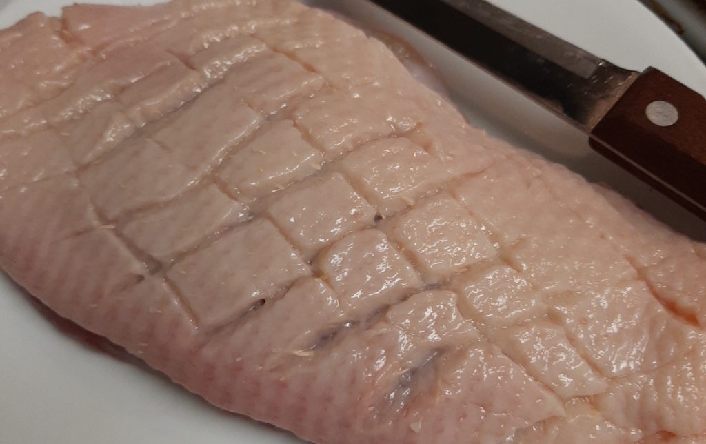 Scored skin and fat on a duck breast to prepare for cooking.