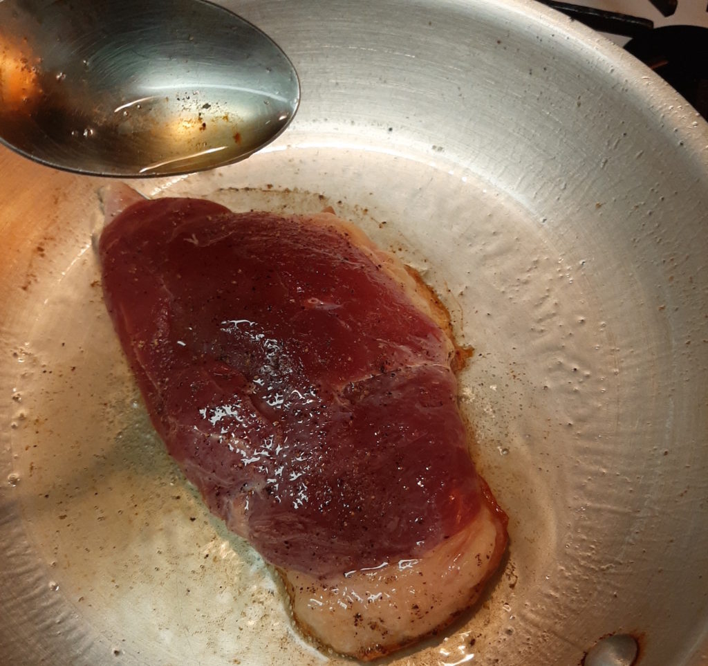 Pan-seared Duck Breast, skin-side down in a cold pan, reducing fat in the skin and forming a crust. Spooning released fat over the raw meat.