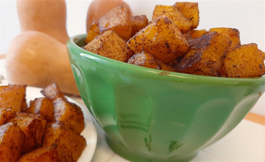 Roasted butternut squash in green bowl and plate with cardamom and winter spices surrounded with butternut squash.