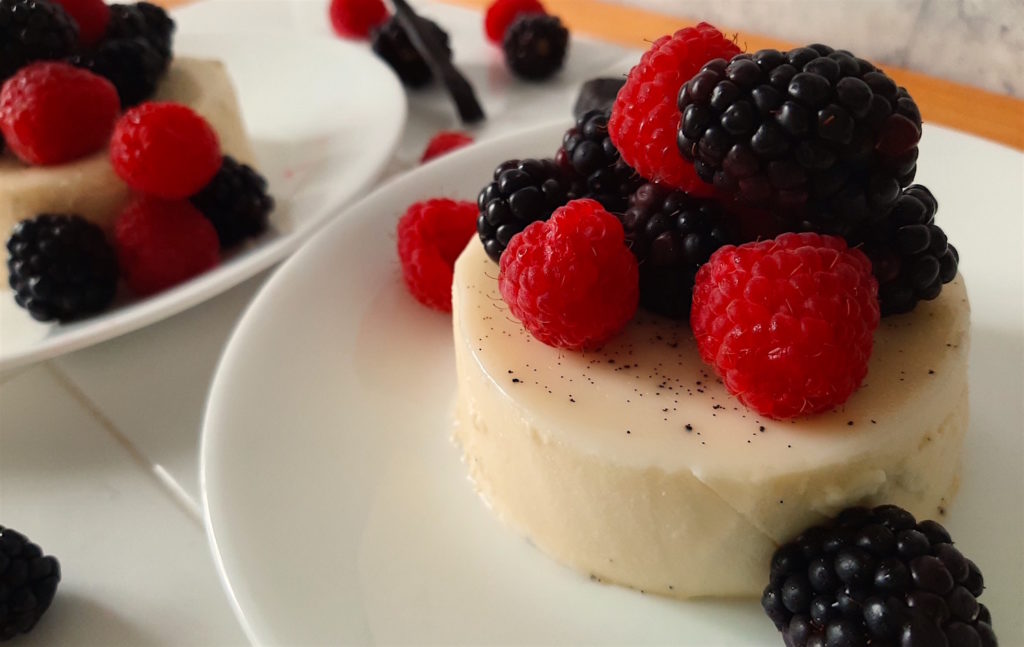 Vanilla Bean Panna Cotta with fresh Raspberries and Blackberries. Vanilla bean and more fresh berries in the background.