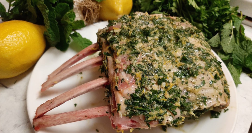 Raw half rack of lamb with marinade of lemons, mint, and garlic.