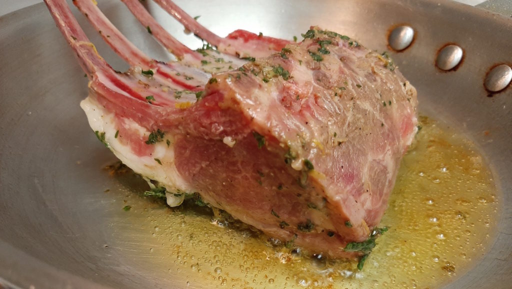 Raw half rack of lamb searing in a pan before roasting.