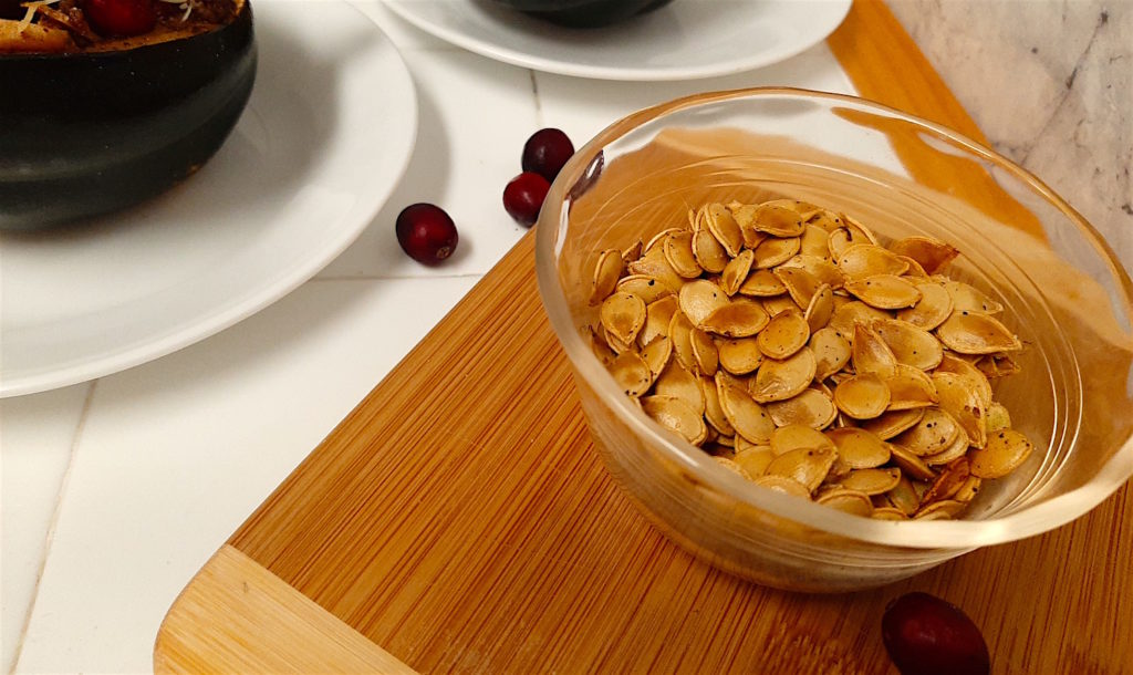 Acorn squash seeds with two stuffed acorn squash in the background and cranberries around.