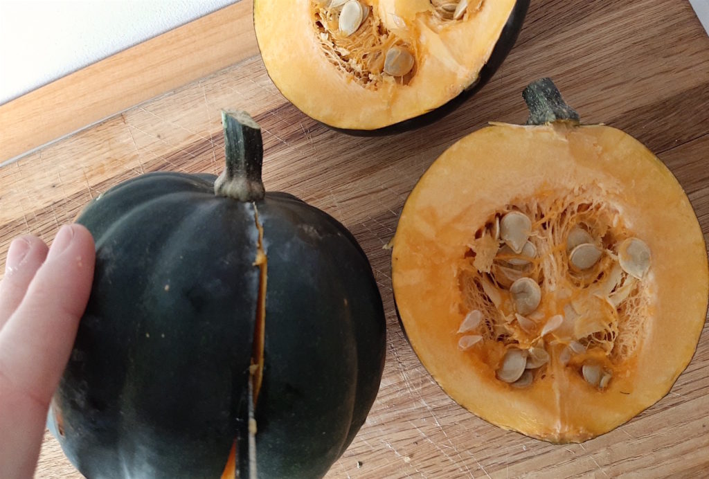 How to cut an acorn squash, cutting a squash in half with one already cut showing acorn squash seeds.