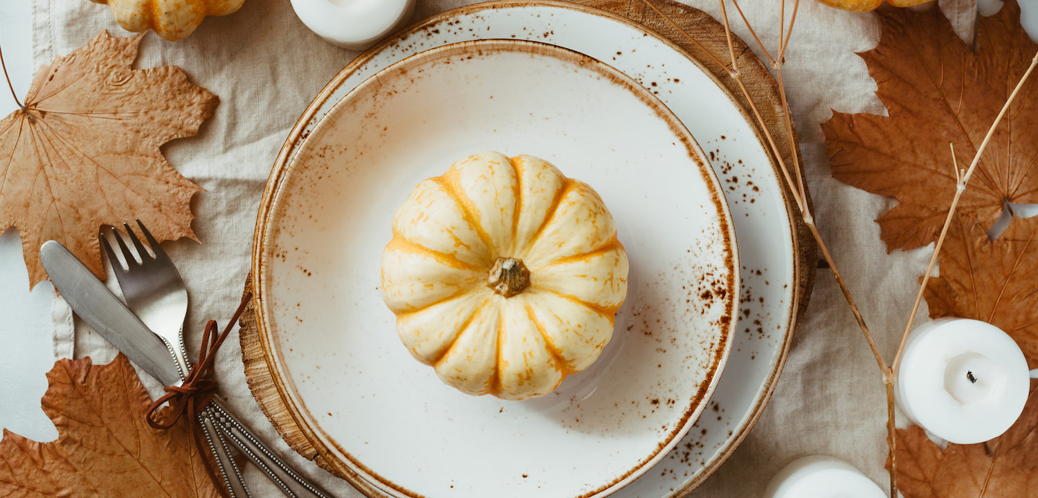 Fall Table Spread with pumpkin on white plate surrounded by white candles and maple leaves