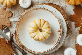 Fall Table Spread with pumpkin on white plate surrounded by white candles and maple leaves