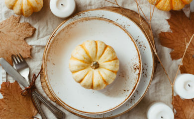 Fall Table Spread with pumpkin on white plate surrounded by white candles and maple leaves