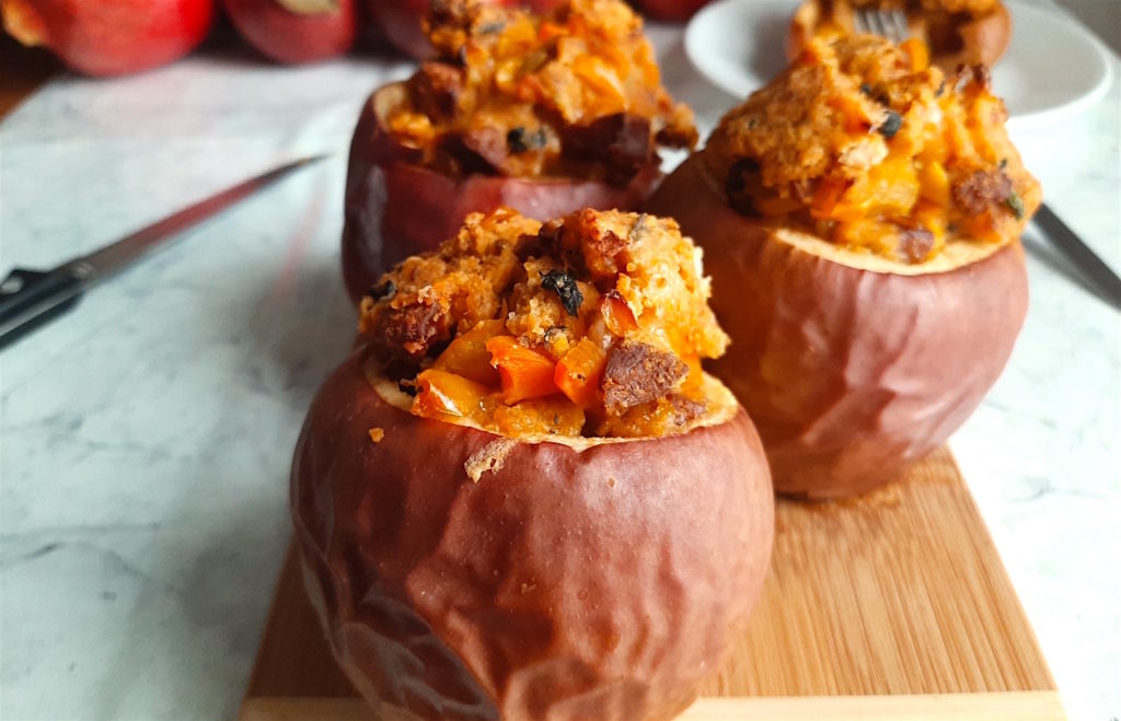 Three savory stuffed apples with Chorizo and Cornbread stuffing on a wooden cutting board with apples and a sliced apple in the background. Sugar with Spice Blog