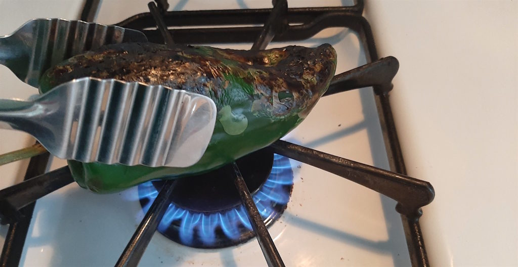 Poblano Pepper blackening skin over open gas stove with metal tongs