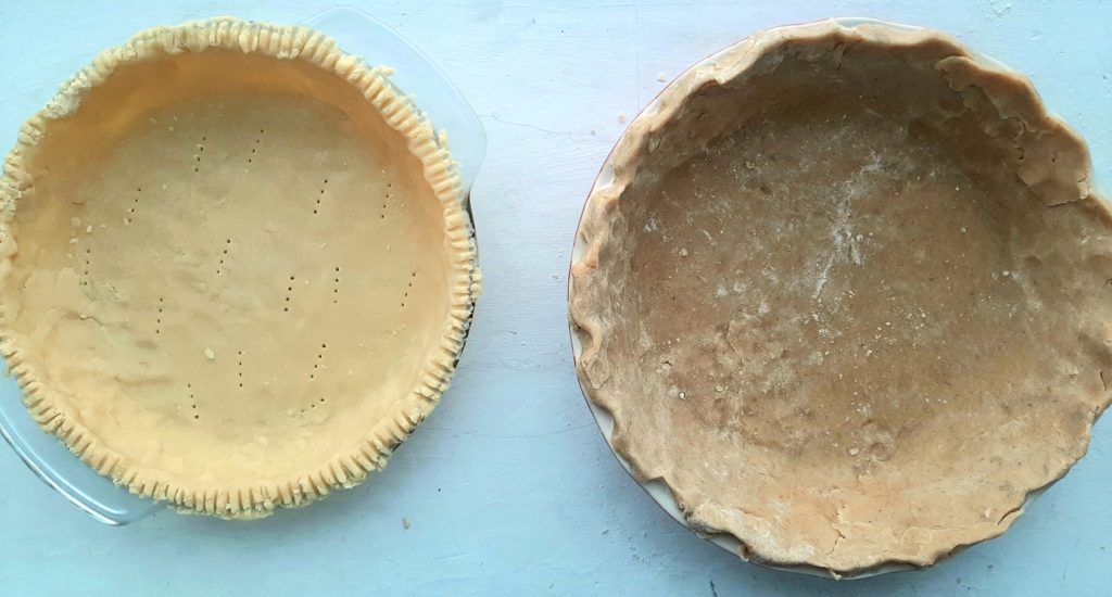 Raw all-butter pie crusts shaped and ready for filling. Regular all-butter pie crust in a glass pan with fork pressed edges. Spiced all-butter pie crust in a red ceramic dish with crimped edges.