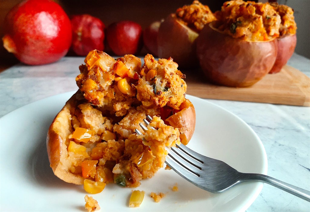 Sliced savory stuffed apple with Chorizo and Cornbread stuffing on a plate with a fork, more stuffed and whole apples in the background. Sugar with Spice Blog