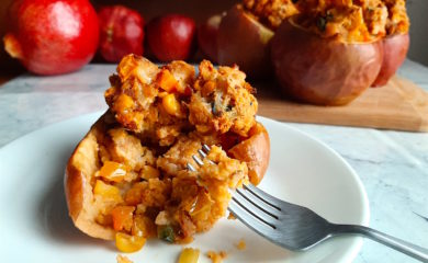 Sliced savory stuffed apple with Chorizo and Cornbread stuffing on a plate with a fork, more stuffed and whole apples in the background. Sugar with Spice Blog