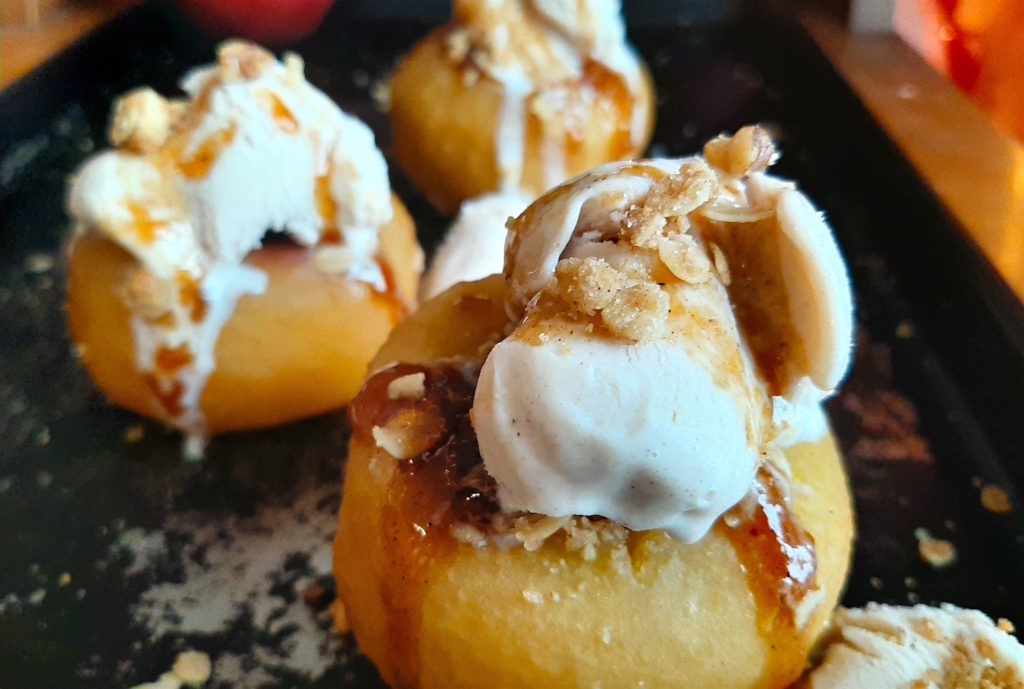 Sherry Poached Apples with Crumb Topping filling and Cinnamon Gelato covered in a sherry glaze on a baking dish with apples in the background. Sugar with Spice Blog.