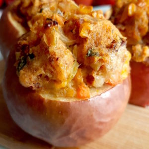 Three savory stuffed apples with Chorizo and Cornbread stuffing on a wooden cutting board with apples and a sliced apple in the background. Sugar with Spice Blog