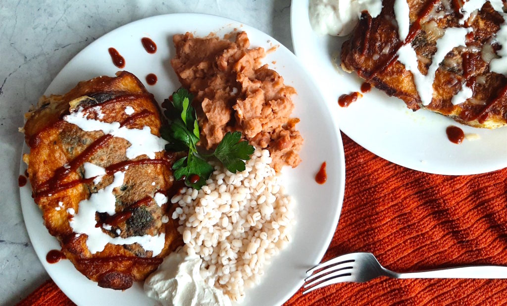 Shrimp and butternut squash stuffed poblano peppers on a white plate with refried beans and barley, drizzled with siracha and sour cream and cilantro. Sugar with Spice Blog.