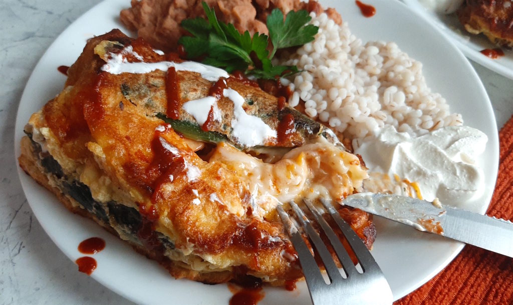 Shrimp and butternut squash stuffed poblano peppers on a white plate with refried beans and barley, drizzled with siracha and sour cream and cilantro. Sugar with Spice Blog.