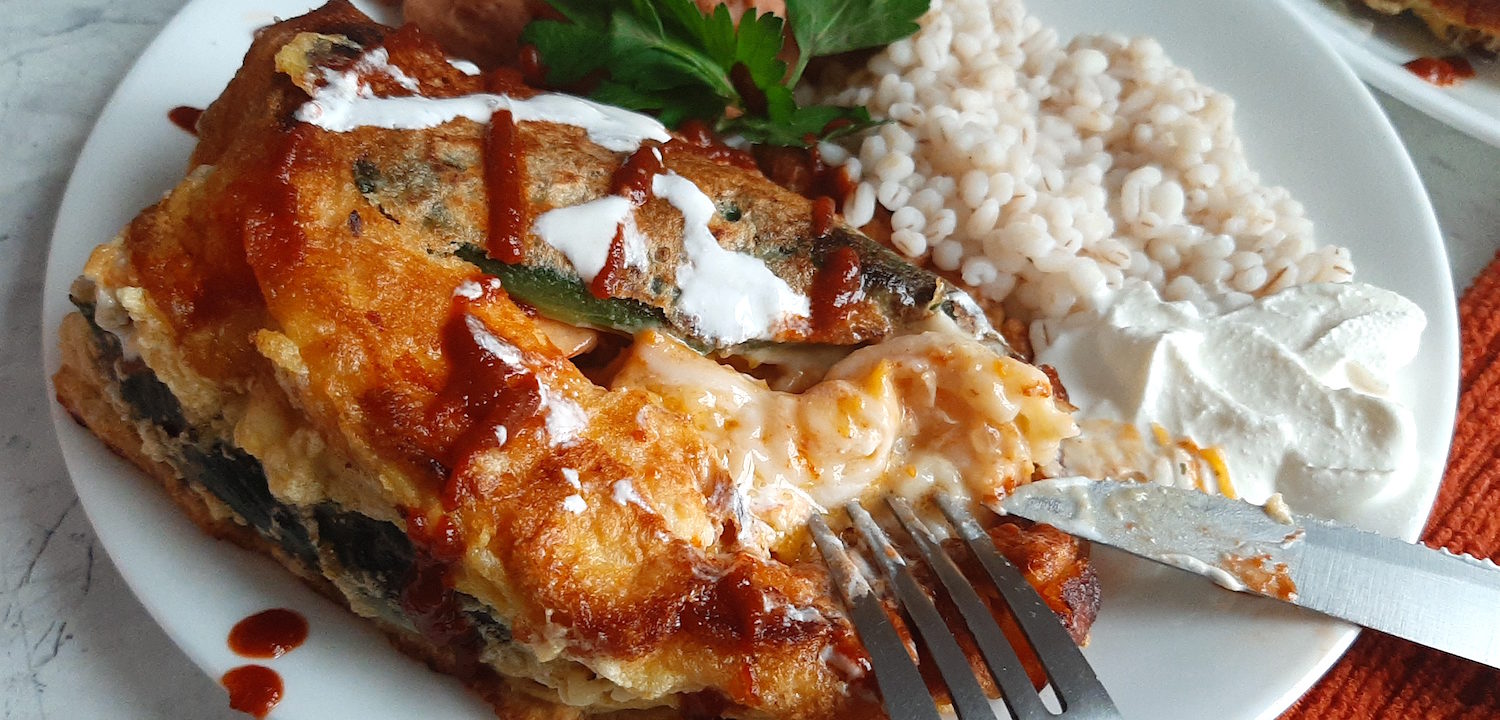 Shrimp and butternut squash stuffed poblano peppers on a white plate with refried beans and barley, drizzled with siracha and sour cream and cilantro. Sugar with Spice Blog.