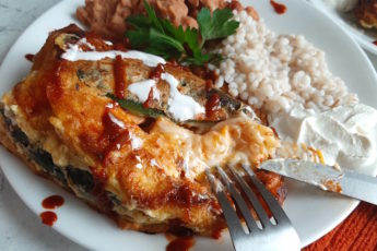 Shrimp and butternut squash stuffed poblano peppers on a white plate with refried beans and barley, drizzled with siracha and sour cream and cilantro. Sugar with Spice Blog.