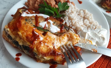 Shrimp and butternut squash stuffed poblano peppers on a white plate with refried beans and barley, drizzled with siracha and sour cream and cilantro. Sugar with Spice Blog.