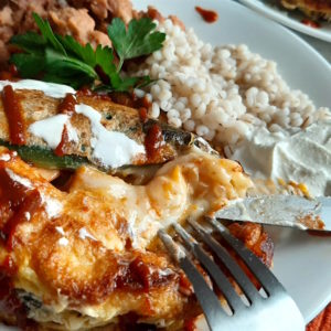 Shrimp and butternut squash stuffed poblano peppers on a white plate with refried beans and barley, drizzled with siracha and sour cream and cilantro. Sugar with Spice Blog.