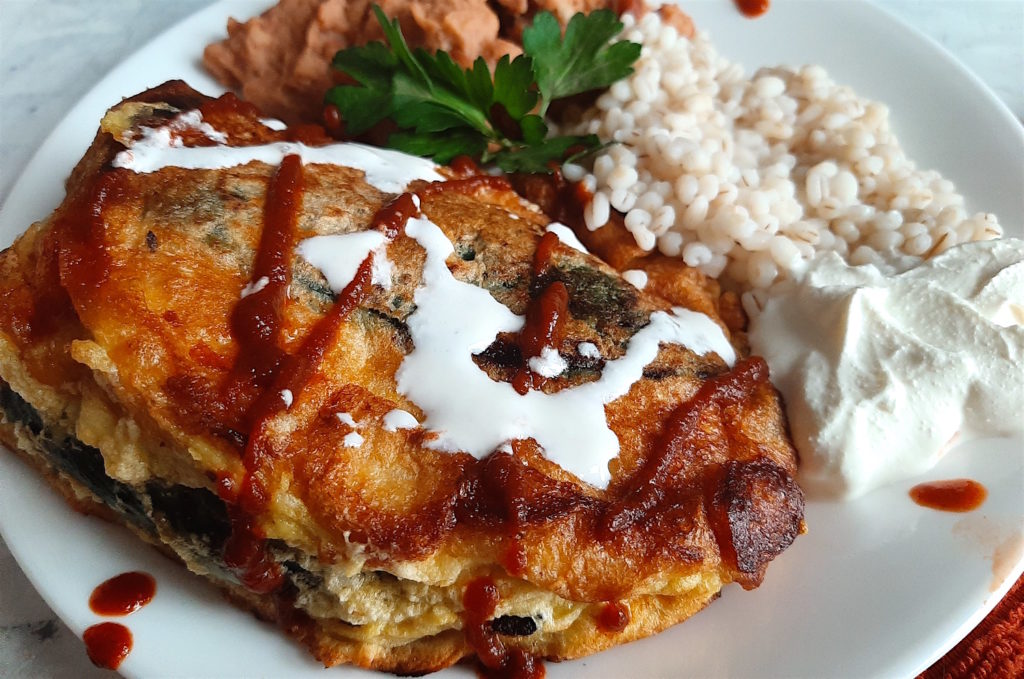 Shrimp and butternut squash stuffed poblano peppers on a white plate with refried beans and barley, drizzled with siracha and sour cream and cilantro. Sugar with Spice Blog.