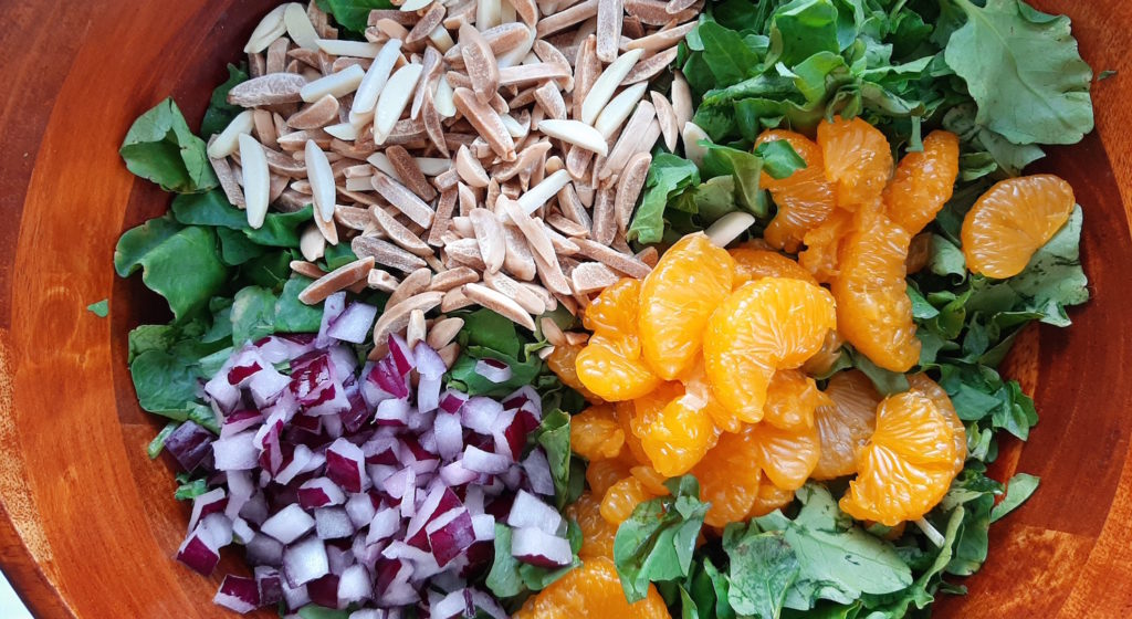 Watercress with mandarin oranges, toasted almonds, red onions in a dark wood bowl, separated ingredients