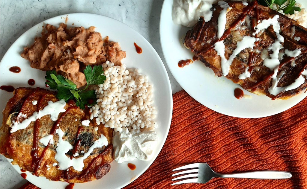 Shrimp and butternut squash stuffed poblano peppers on a white plate with refried beans and barley, drizzled with siracha and sour cream and cilantro. Sugar with Spice Blog.
