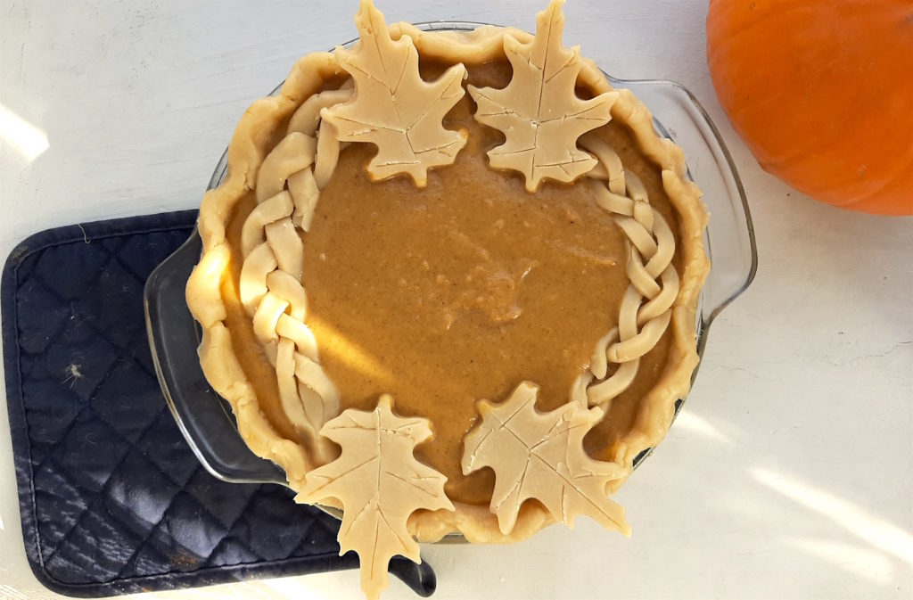 All-butter pie crust and fresh pumpkin pie in a glass dish, raw, ready to go in the oven. With an oven mitt and pumpkin. Sugar with Spice Blog