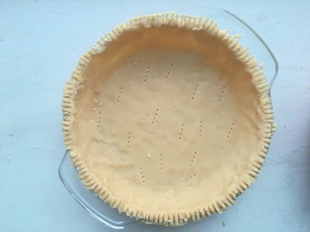 Regular all-butter pie crust raw in a glass dish with fork pressed edges and fork pricks. Sugar with Spice Blog