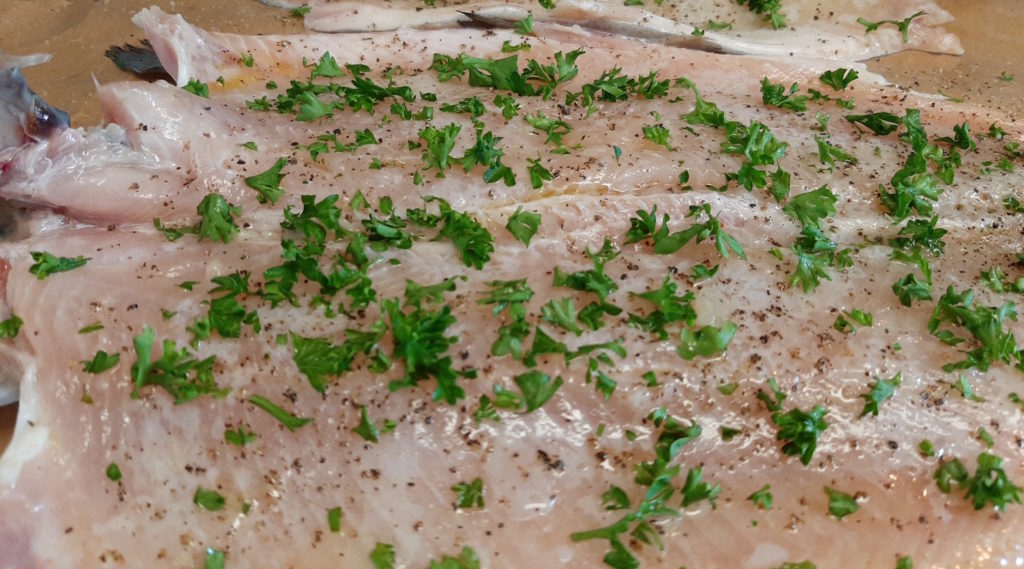 Whole Rainbow trout seasoned with lemon, pepper, and fresh parsley, inside of fish