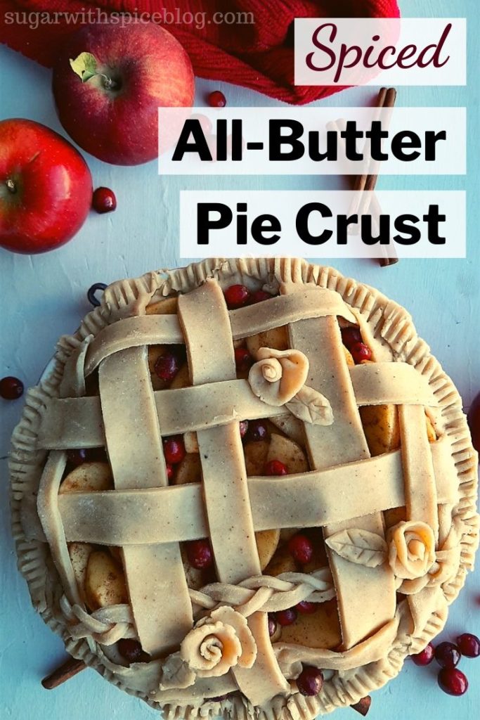 Spiced All-Butter Pie Crust pinterest image, spiced cranberry apple pie with spiced all-butter pie crust raw in a ceramic dish with lattice braided crust and rose designs ready to go into the oven. Surrounded by apples, cranberries, cinnamon stick, and red kitchen towel. Sugar with Spice Blog.