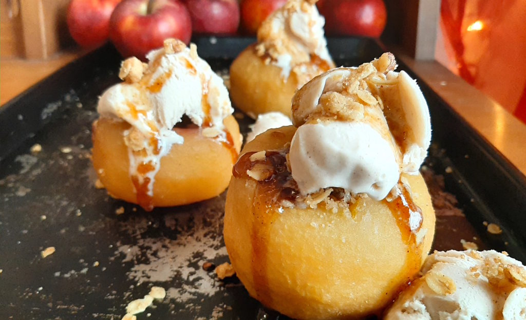 Sherry Poached Apples with Crumb Topping filling and Cinnamon Gelato covered in a sherry glaze on a baking dish with apples in the background. Sugar with Spice Blog.