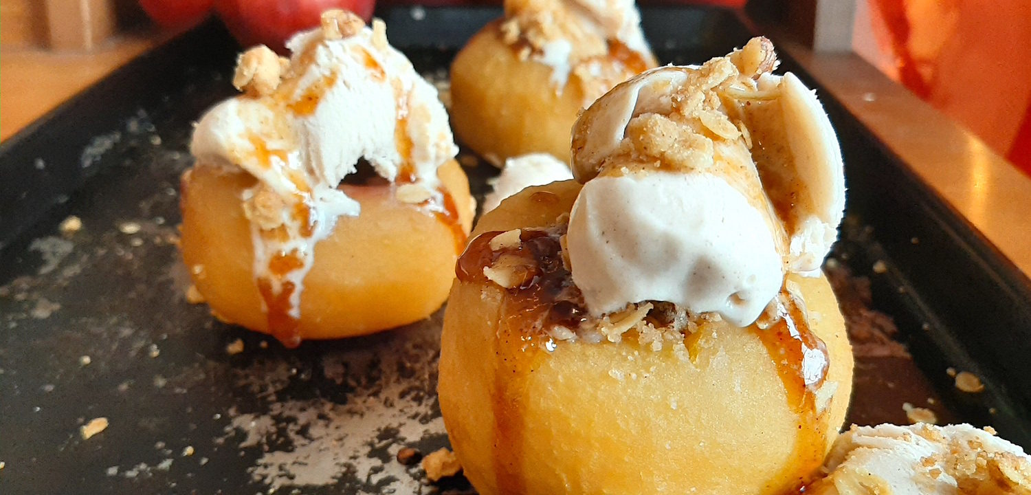 Sherry Poached Apples with Crumb Topping filling and Cinnamon Gelato covered in a sherry glaze on a baking dish with apples in the background. Sugar with Spice Blog.