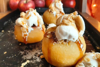 Sherry Poached Apples with Crumb Topping filling and Cinnamon Gelato covered in a sherry glaze on a baking dish with apples in the background. Sugar with Spice Blog.