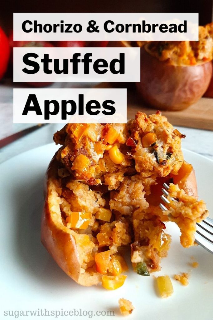Savory stuffed apples with Chorizo and Cornbread stuffing sliced open with a fork on a white plate with more stuffed apples on a wooden cutting board in the background. Sugar with Spice Blog