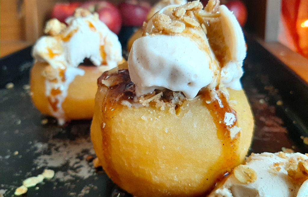 Sherry Poached Apples with Crumb Topping filling and Cinnamon Gelato covered in a sherry glaze on a baking dish with apples in the background. Sugar with Spice Blog.