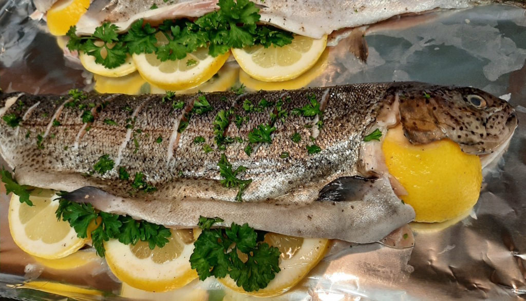 Whole Rainbow trout seasoned and stuffed with lemon, pepper, and fresh parsley on tinfoil