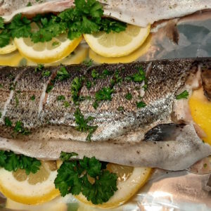 Whole Rainbow trout seasoned and stuffed with lemon, pepper, and fresh parsley on tinfoil