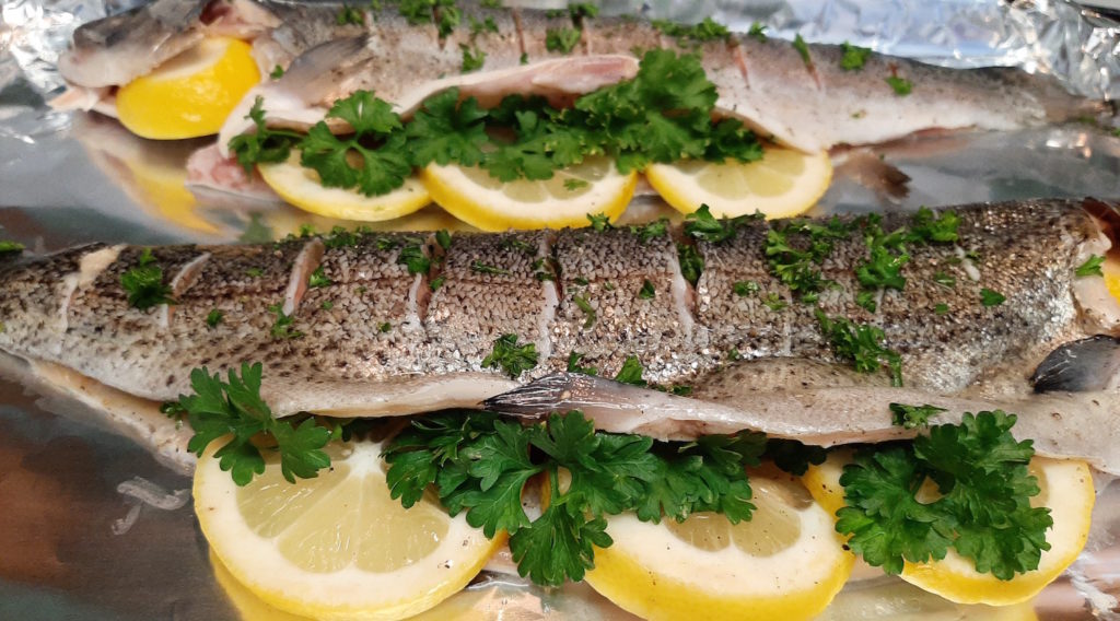 Whole Rainbow trout seasoned and stuffed with lemon, pepper, and fresh parsley on tinfoil